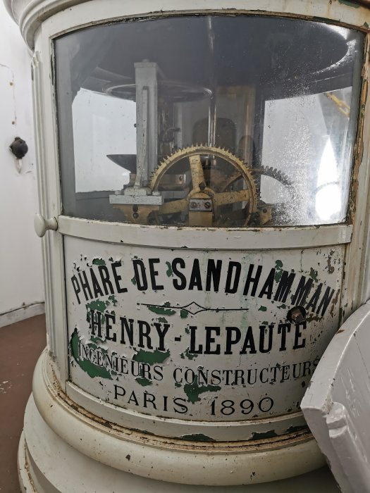 Del av ett gammalt fyrverk med mekaniska kugghjul och texten 'Phare De Sandhammam Henry Lepaute Ingenieurs Constructeurs Paris 1890'.