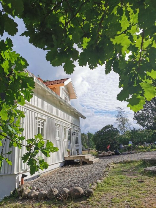 Nyrenoverat vitmålat hus med borttagen byggställning, stenfasad och grönska, under klart himmel.