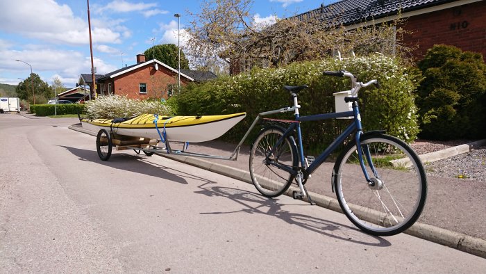 Cykel med hemmagjord kanotvagn som transporterar en gul och vit kajak på en stadsgata.