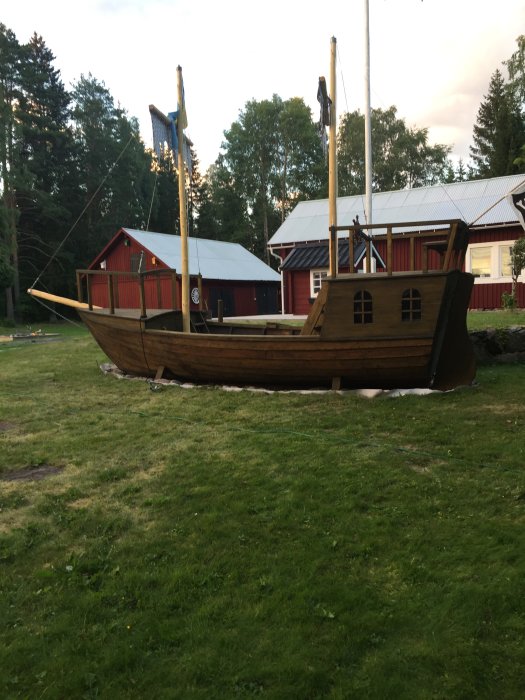 Träleksakskepp i nästan full storlek i en trädgård med hus i bakgrunden.