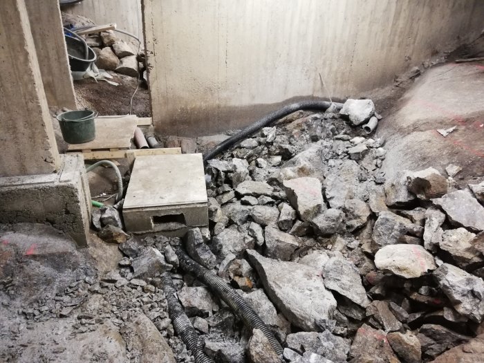 En byggarbetsplats med återfyllda stenmaterial och betongrör, synliga kablar och byggspill.