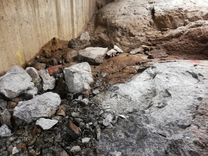 Grus och stora stenblock vid en grävd grop som visar påbörjad återfyllning av material.
