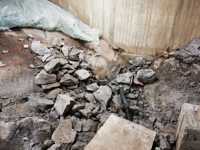 Återfyllning av grävd byggplats med betongrester och grus bland byggmaterial och jord.