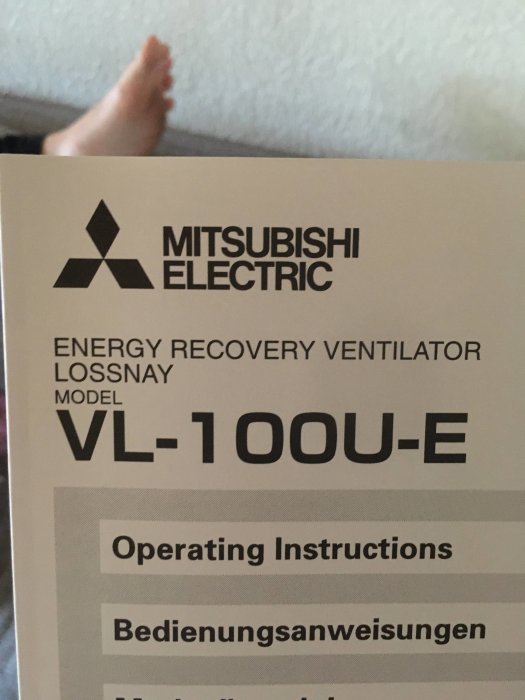 Etikett på en Mitsubishi Electric Energy Recovery Ventilator, modell VL-100U-E, med en fot i bakgrunden.