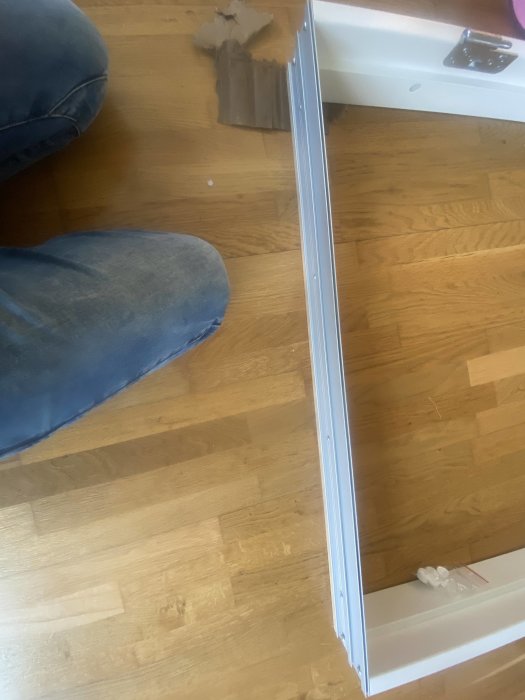 Dörrtröskel till synes svårfäst vid trägolv, med byggavfall och användares ben.