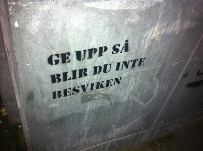 Spraymålad text "GE UPP SÅ BLIR DU INTE BESVIKEN" på en smutsig yta.