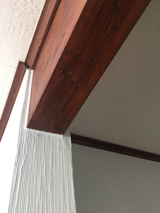 En træbjælke monteret på en hvidmalet væg, set nedefra. Bjælken er en del af en bærende konstruktion.