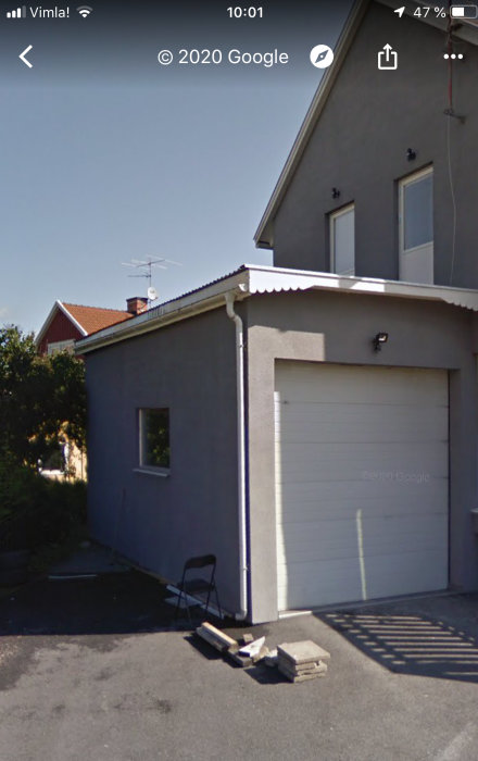 Garage på hus med stängd vit garageport, antenn på taket och byggmaterial framför.