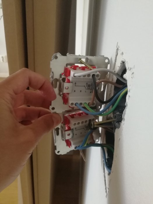 Hand som håller en singel väggbrytare med synliga ledningar och anslutningar i en öppen vägginstallation.