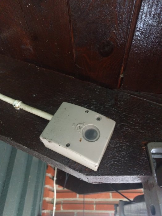 Ett skymningsrelä installerat under en mörkbrun trälist.