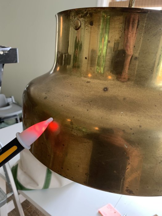 Begagnad Bumling lampa i mässing testas med elpenna som lyser rött vid kontakt, indikerar potentiell elektrisk fara.
