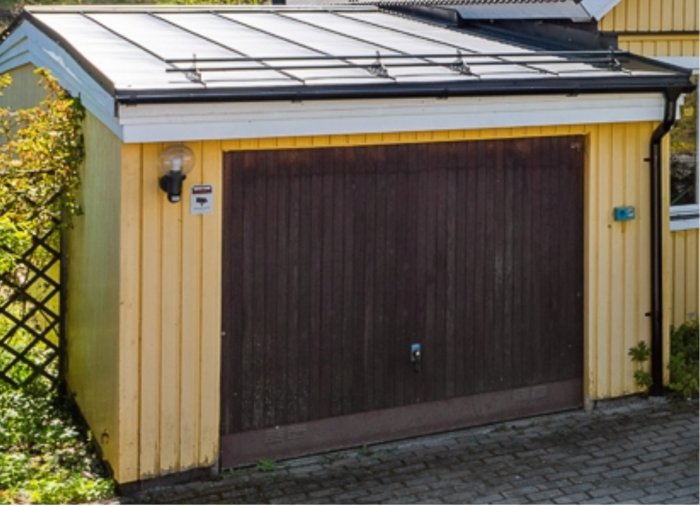 Ett gult garage med brun dörr byggt 1979, står på tryckimpregnerade syllar med synliga rötskador.