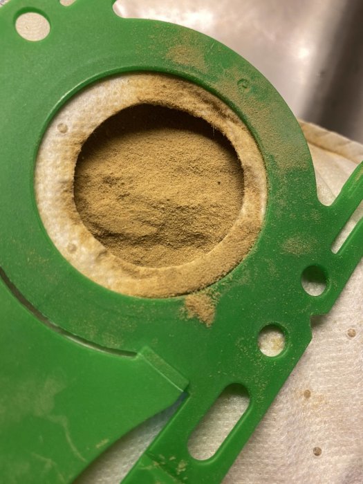 Öppningen av en dammsugarpåse med fint damm från en 70-tals matta, inga synliga trådar.