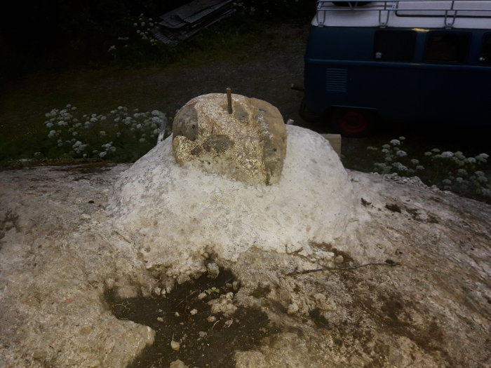 Betongfundament med järnstänger för stolpinfästning framför en blå husbil.