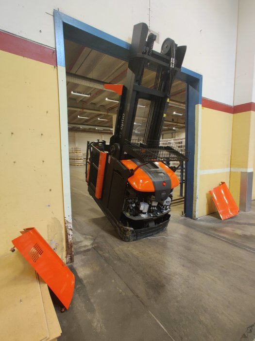 Orange svart gaffeltruck framför en blå dörröppning, delar av trucken ligger löst på golvet.