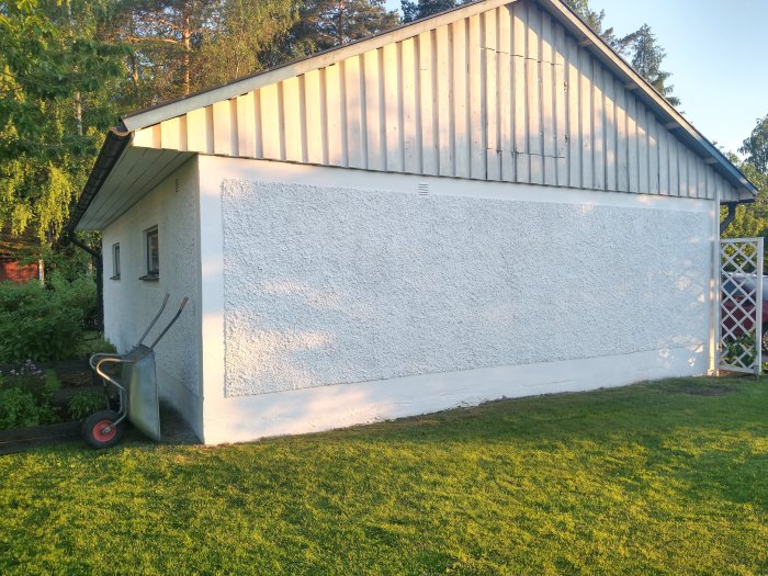 Nymålad putsad garagevägg med färgspruta och trävirket på vindskivan i bakgrunden.