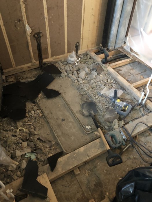 Renoveringsprojekt av badrum med uppbilat golv, exponerade rör och verktyg på plats.
