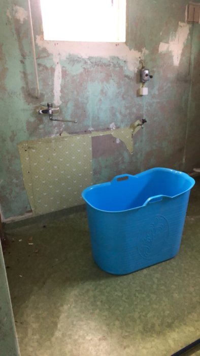 Rivstartat badrum i renoveringsfas med blå balja och avskalade väggar samt golv.