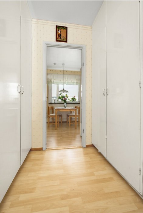 Ljus träklickgolv i en hall med öppen dörr till ett kök, parkettgolv löper i längdriktningen.