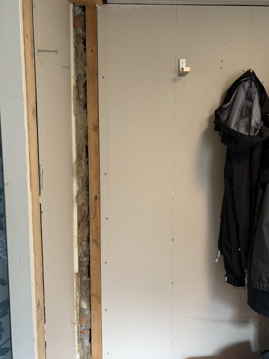 Glipa i väggen efter borttagen garderob i hall, exponerande isolering och träreglar.