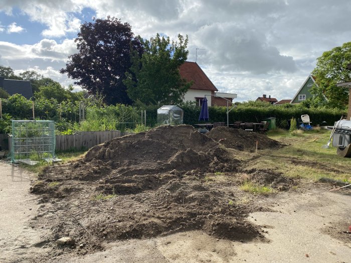 Stor jordhög i en trädgård under anläggning av ny gräsmatta, med hus och växthuset i bakgrunden.