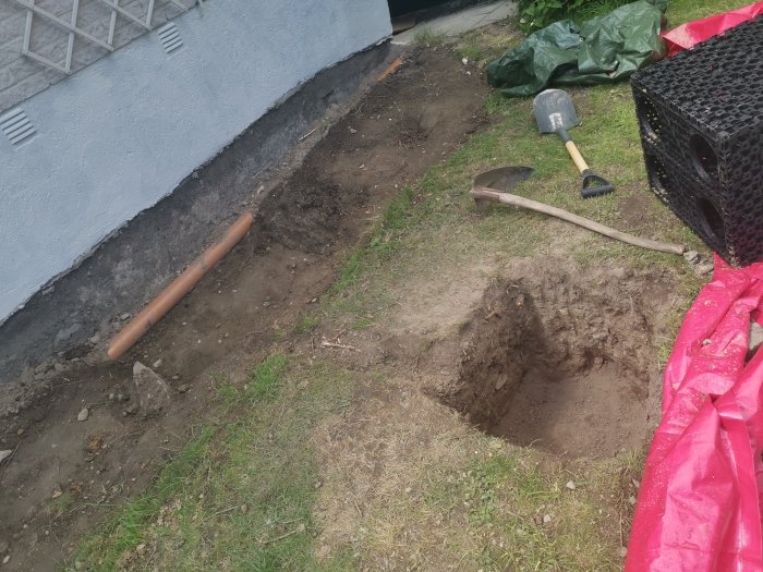 Uppgrävd trädgård för fundament med synligt berg, spadar och dagvattenkassett.