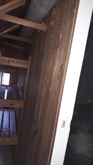 Inre hörn av ett rum med brun väggskiva och träbrädor, inga synliga reglar, vid en trappa.