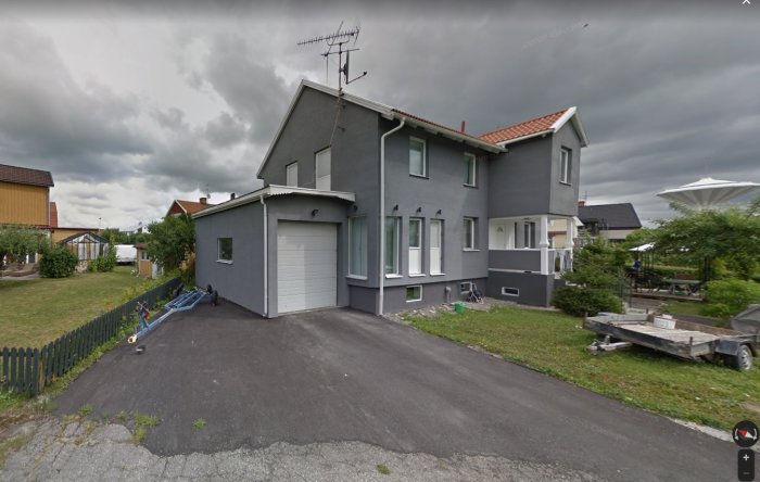 Grått hus med anslutande garage och en dörr på andra våningen indikerar möjlig altan ovanpå garaget.