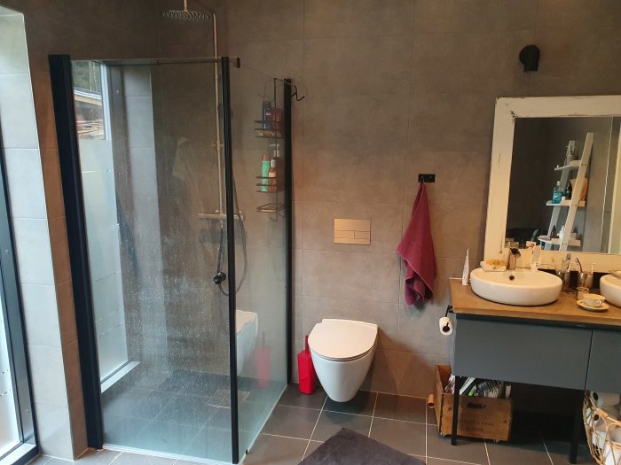 Modern badrum med monterad duschvägg, kommod med stålben och toapappershållare på kommoden.