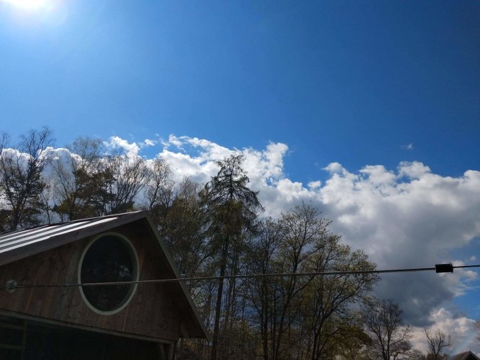 Linbana fäst vid ett trädgårdsskjul med förstärkta stålbalkar, blå himmel med moln i bakgrunden.