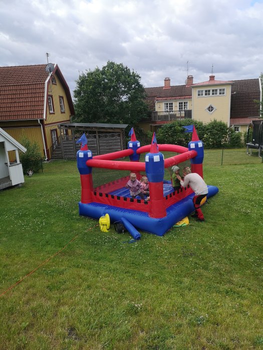 En färgglad hoppborg för barn i en trädgård med hus och träd i bakgrunden.