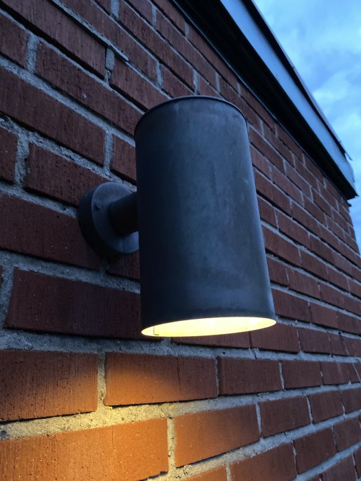 Vägglampa i cylinderformat monterad på tegelvägg från 60-talshus.