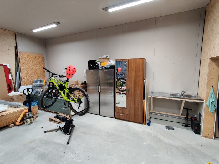 Organiserat garage med cykel i monteringsställ, kyl/frys, diskho och verktyg.