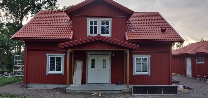 Rödmålat hus i skymningen med nyinstallerad vit pardörr, överljus och fodrar runt garage.