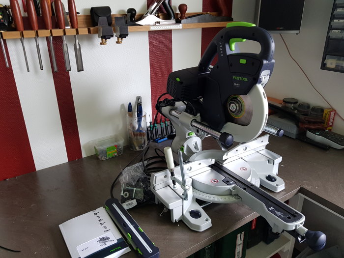 Festool KS60 kap- och geringssåg på arbetsbänk, med verktyg och arbetsredskap i bakgrunden.