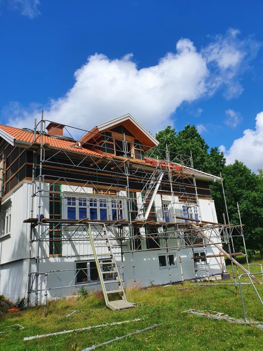 Byggnadsställning uppställd längs baksidan av ett hus under renovering mot blå himmel.