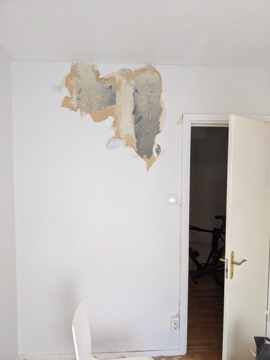 Innervägg med delvis riven tapet som avslöjar ett okänt hårt material undertill.