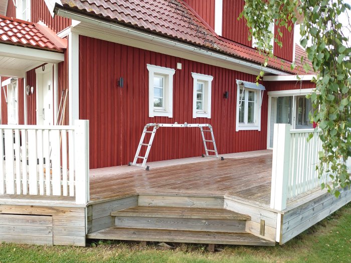 Träveranda på ett rött hus med stege och nyligen utbyggda träläkt.