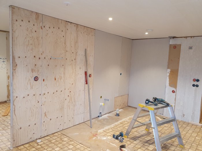 Renoveringsprojekt av kök med plywoodväggar och verktyg, samt golvvärmerör under förberedelse.