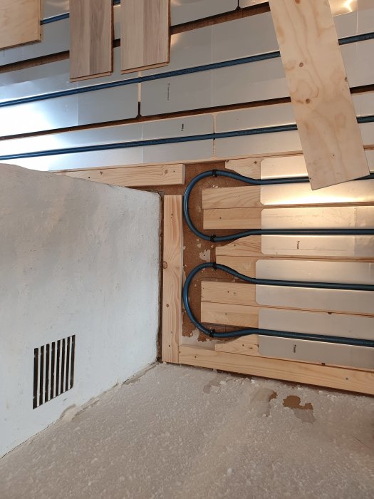 Installation av golvvärmerör och plywood vid gipsvägg under köksrenovering.