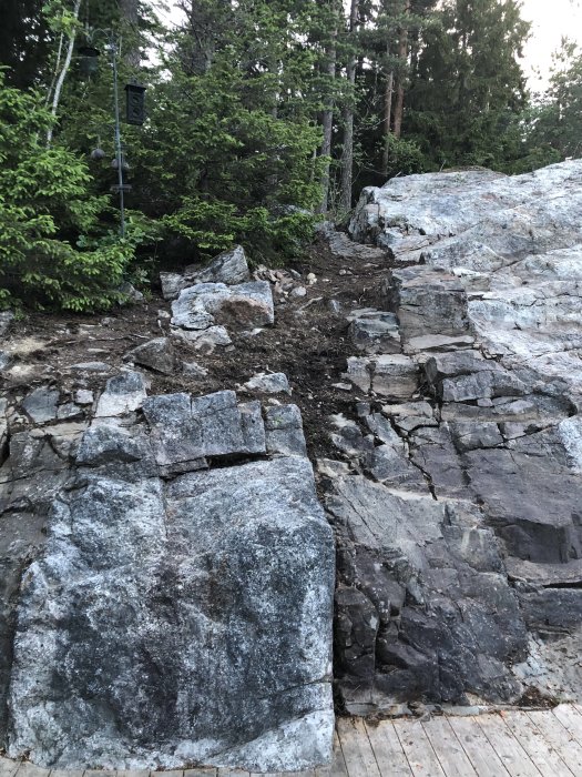 Trädäck intill stenigt berg med synlig lera mellan stenarna efter högtryckstvättning.