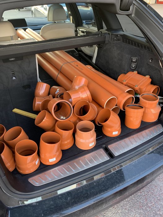 En mängd nya orangea avloppsrör i olika storlekar lastade i bagageutrymmet på en bil.