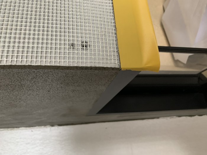 Nyligen putsad yta på en inbyggnad med synligt armeringsnät och skyddad med gul plast.