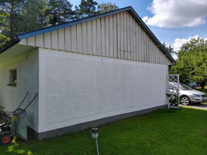 Nymålad vit garagegavel med träpanel och vindskivor, stegar och släpkärra syns i förgrunden.