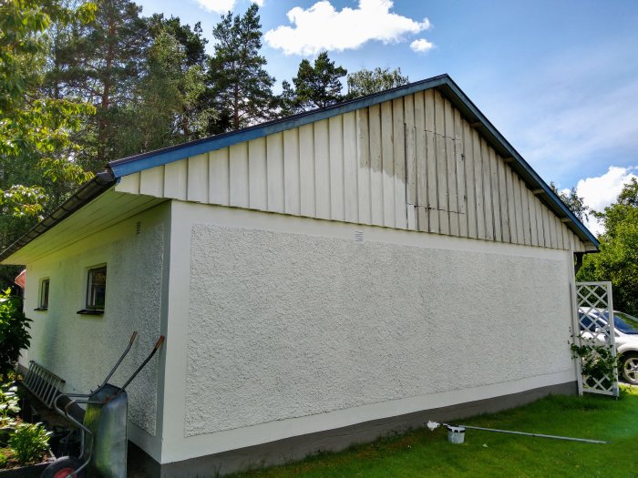 Nyligen målad garagets gavel med vit panel och blå vindskivor, penslar och stegar på marken.