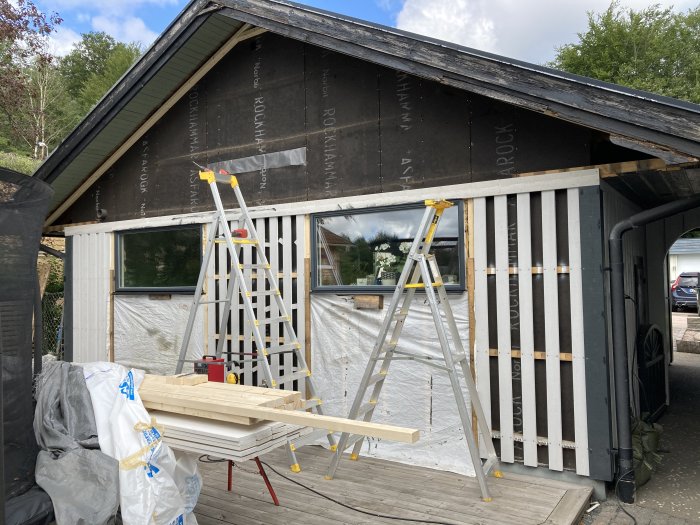 Husvägg under renovering med reglar för liggande panel och torktält för asfabord.