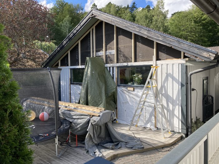 Delvis renoverat hus med ny panel och ett torktält för byggmaterial på terrassen.