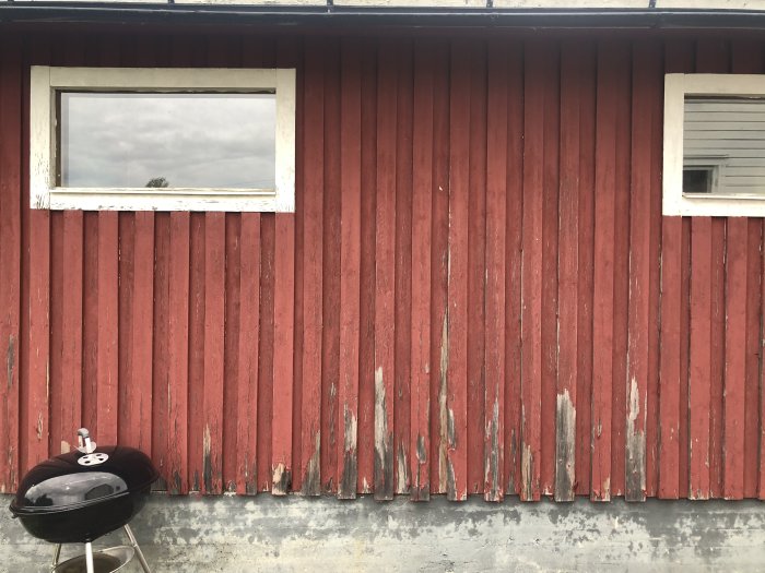 Rödmålat garage med flagnande färg på nedre delen av lockpanelerna, två fönster och en grill framför.