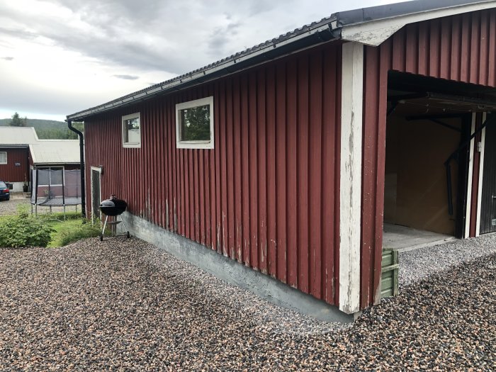 Rödmålat garage med sliten fasad och lockpaneler i behov av underhåll, synligt slitage på nedersta delen.