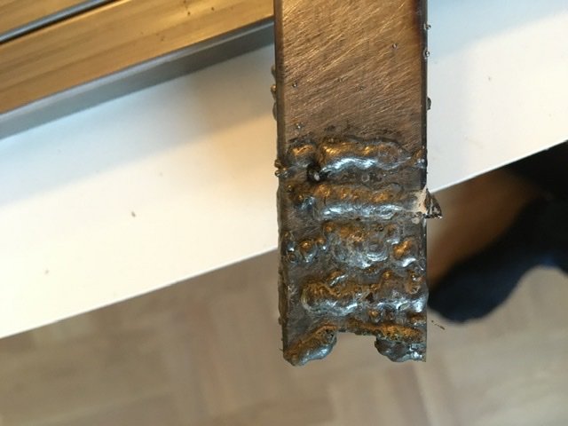 Närbild på ojämn svetsfog på metallrör med synliga svetspärlor och brännskador.